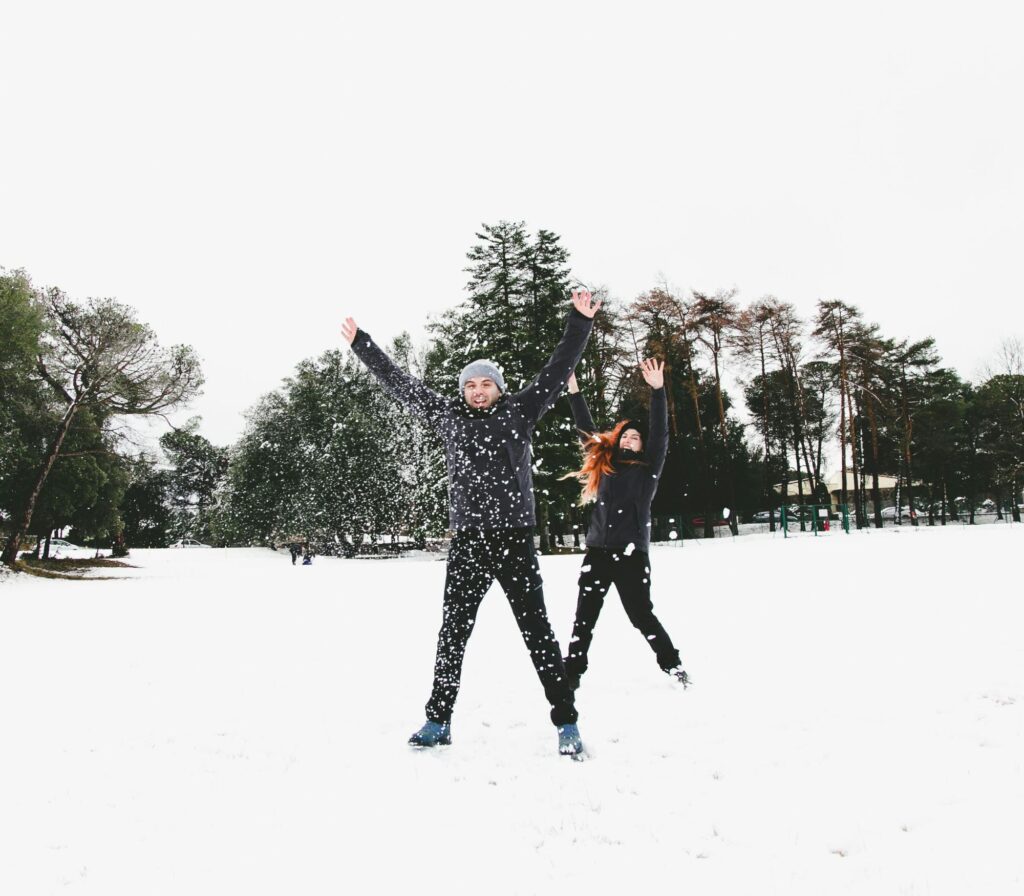 two people, arms extended and throwing snow outside in a an open area