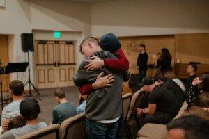 two people hugging in a group room with a podium and speakers
